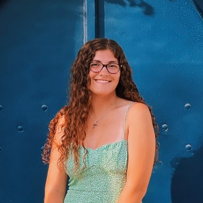 Young woman with long wavy hair smiling wearing teal dress against blue background